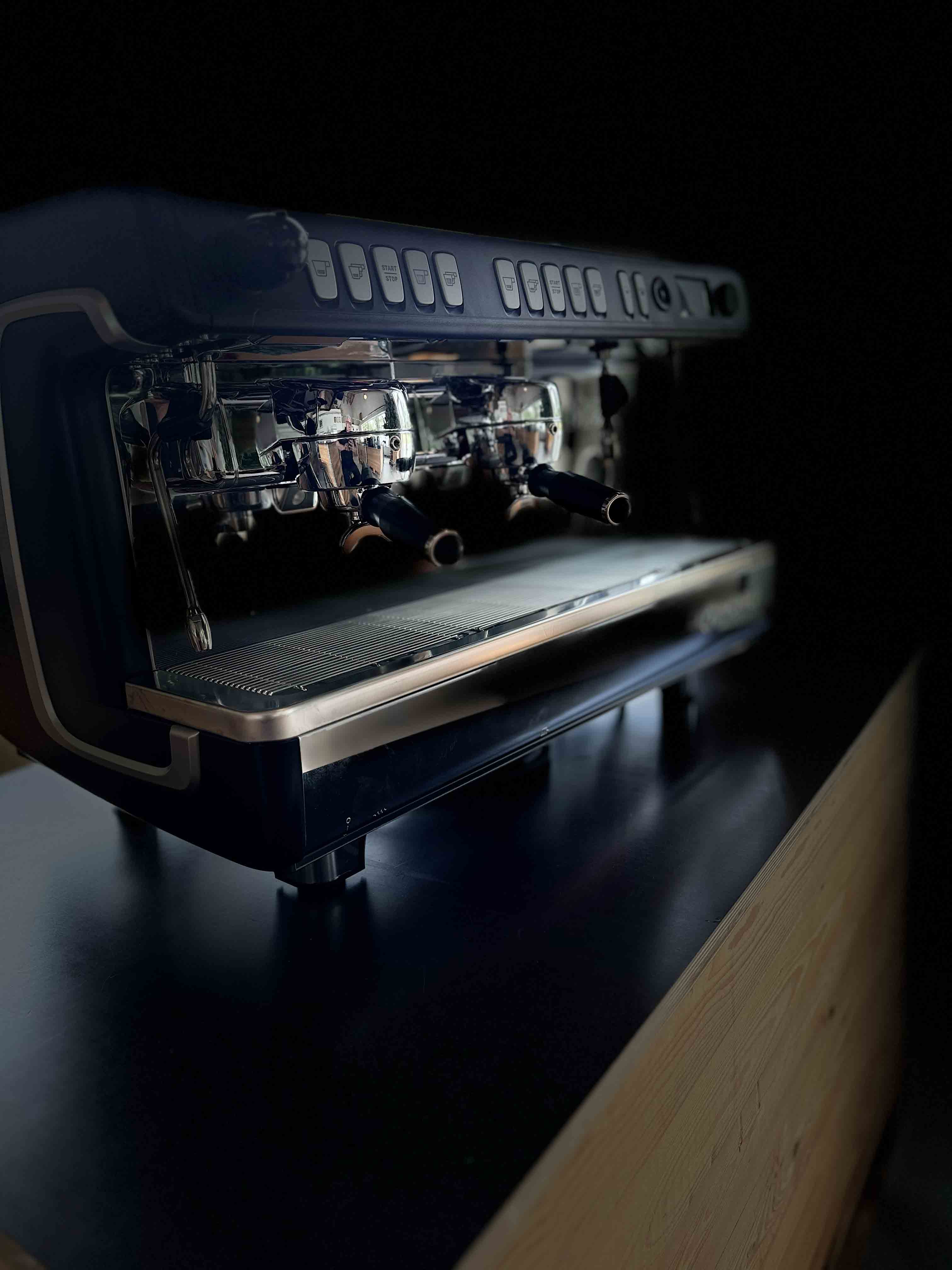 Close-up of a modern dual group espresso machine on a dark countertop with menus on buttons above the group heads.