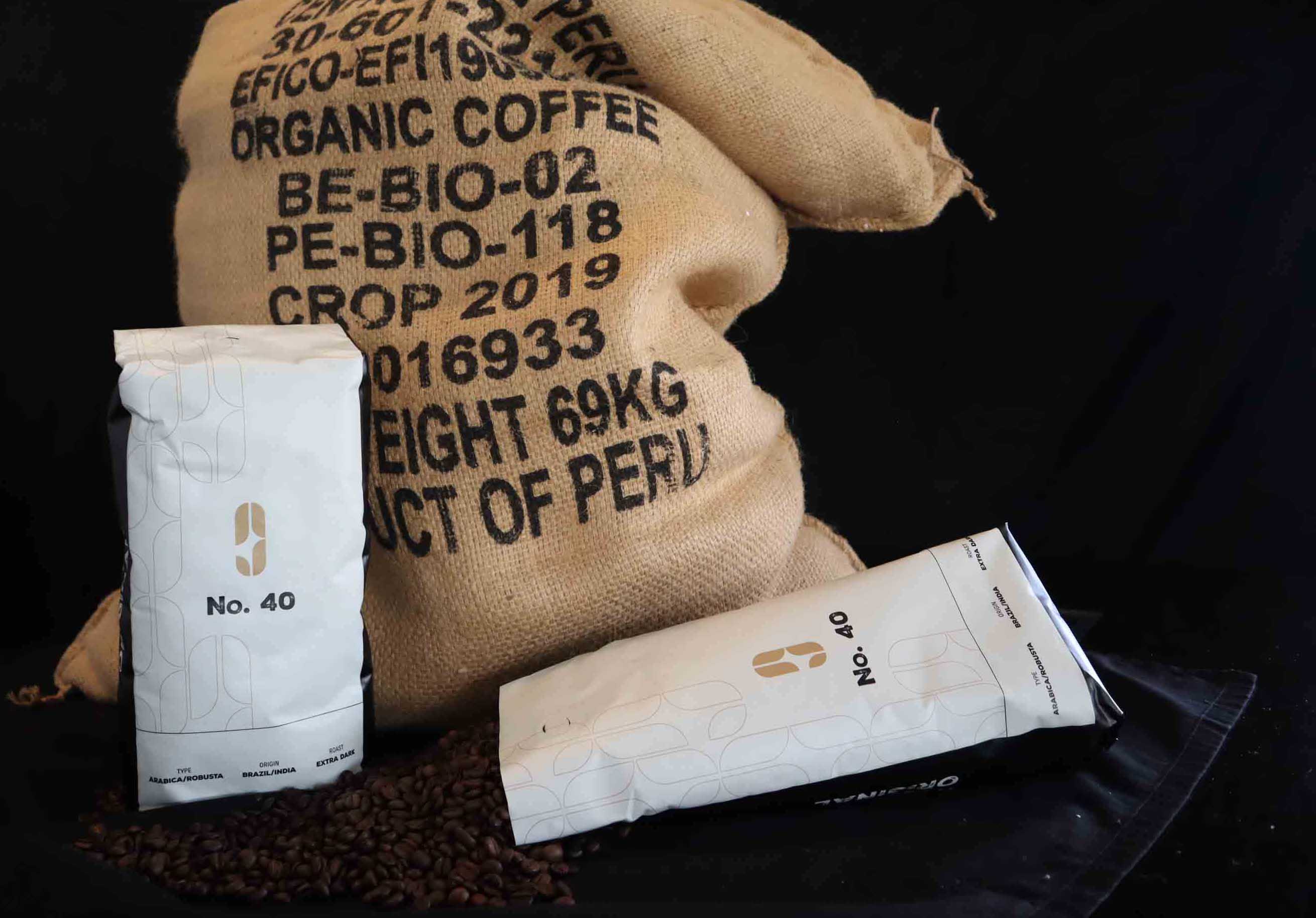 Two white bags labeled No. 40 containing coffee beans, placed near a large burlap sack labeled 'Organic Coffee Product of Peru' on a black background.