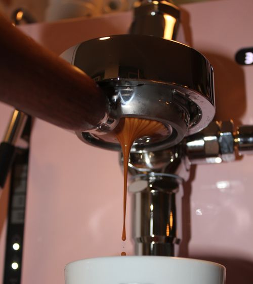 Close-up of espresso flowing from an espresso machine portafilter into a white cup.