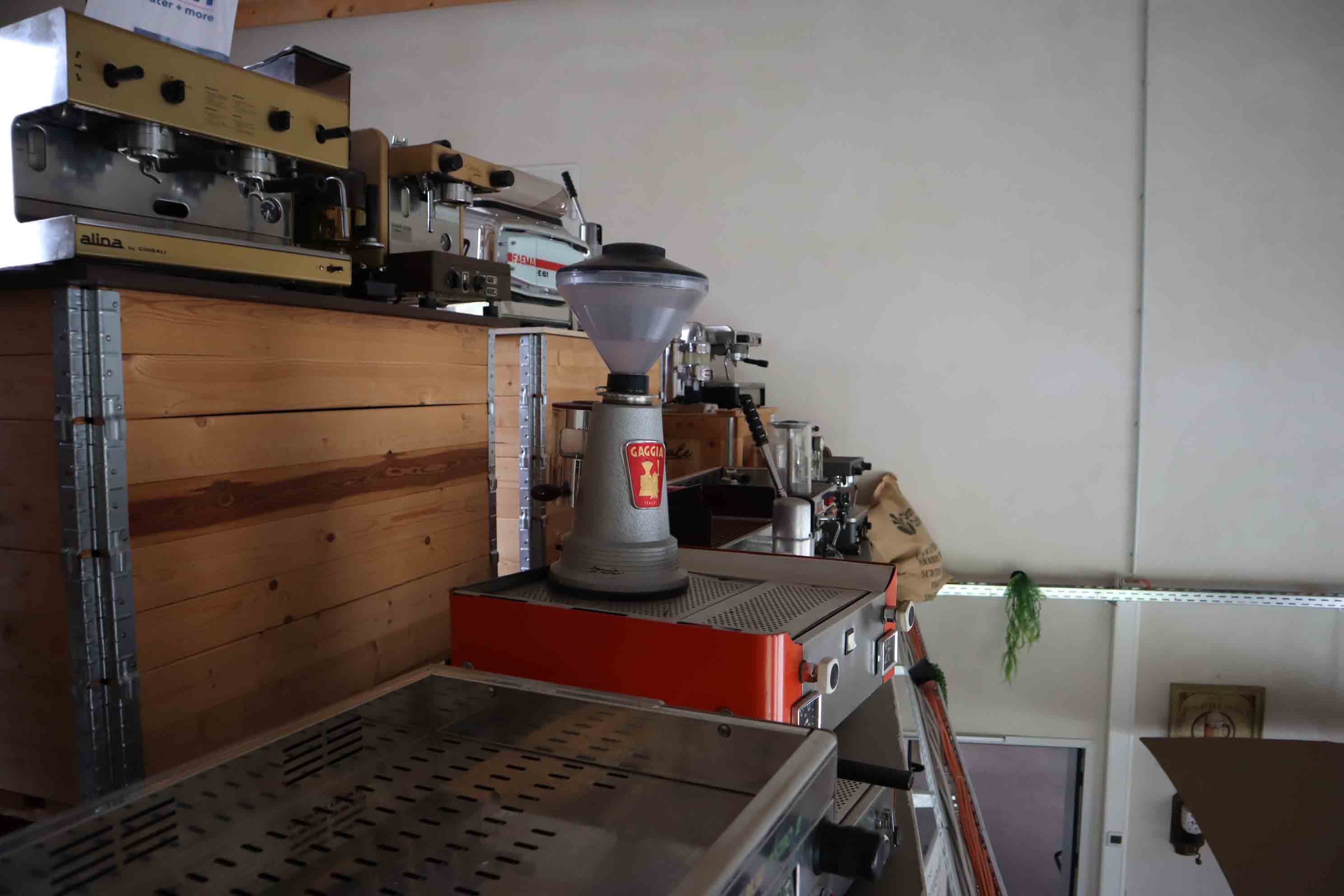A row of vintage espresso machines and coffee grinders displayed on wooden shelves against a white wall.