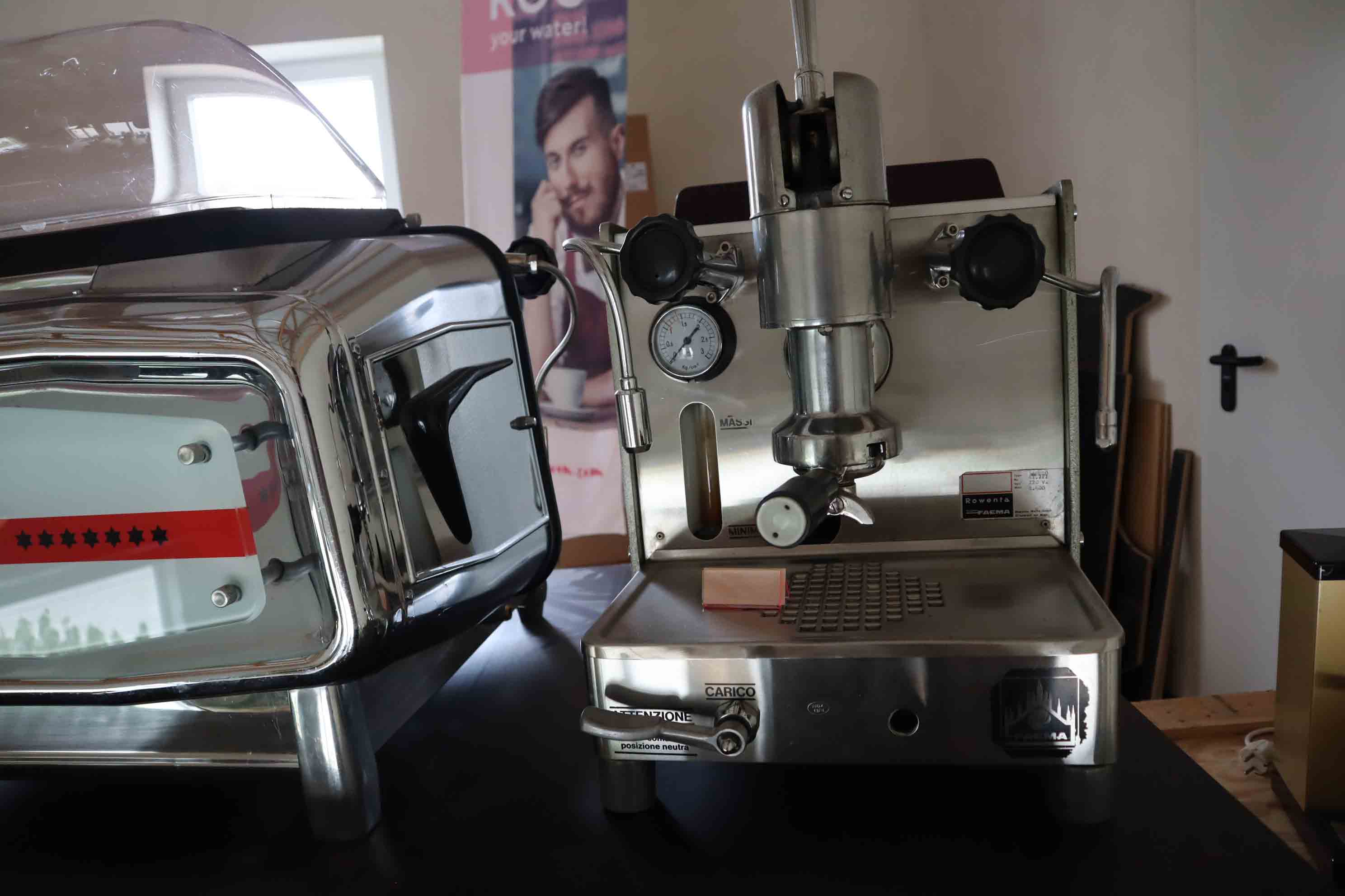 Close-up of a vintage stainless steel espresso machine with pressure gauge and knobs on a dark surface.