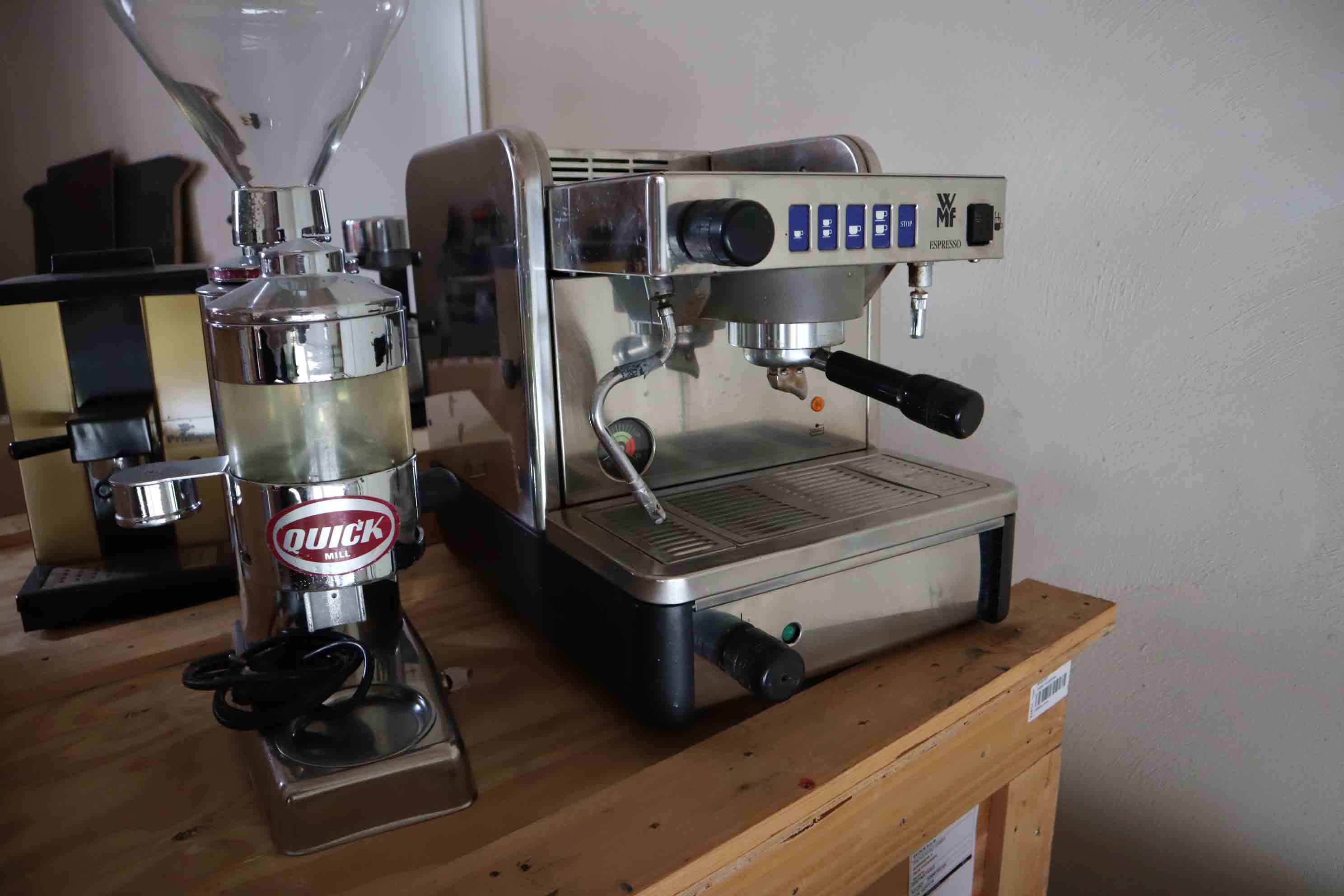 Stainless steel WMF espresso machine and a Quick Mill coffee grinder on a wooden table.