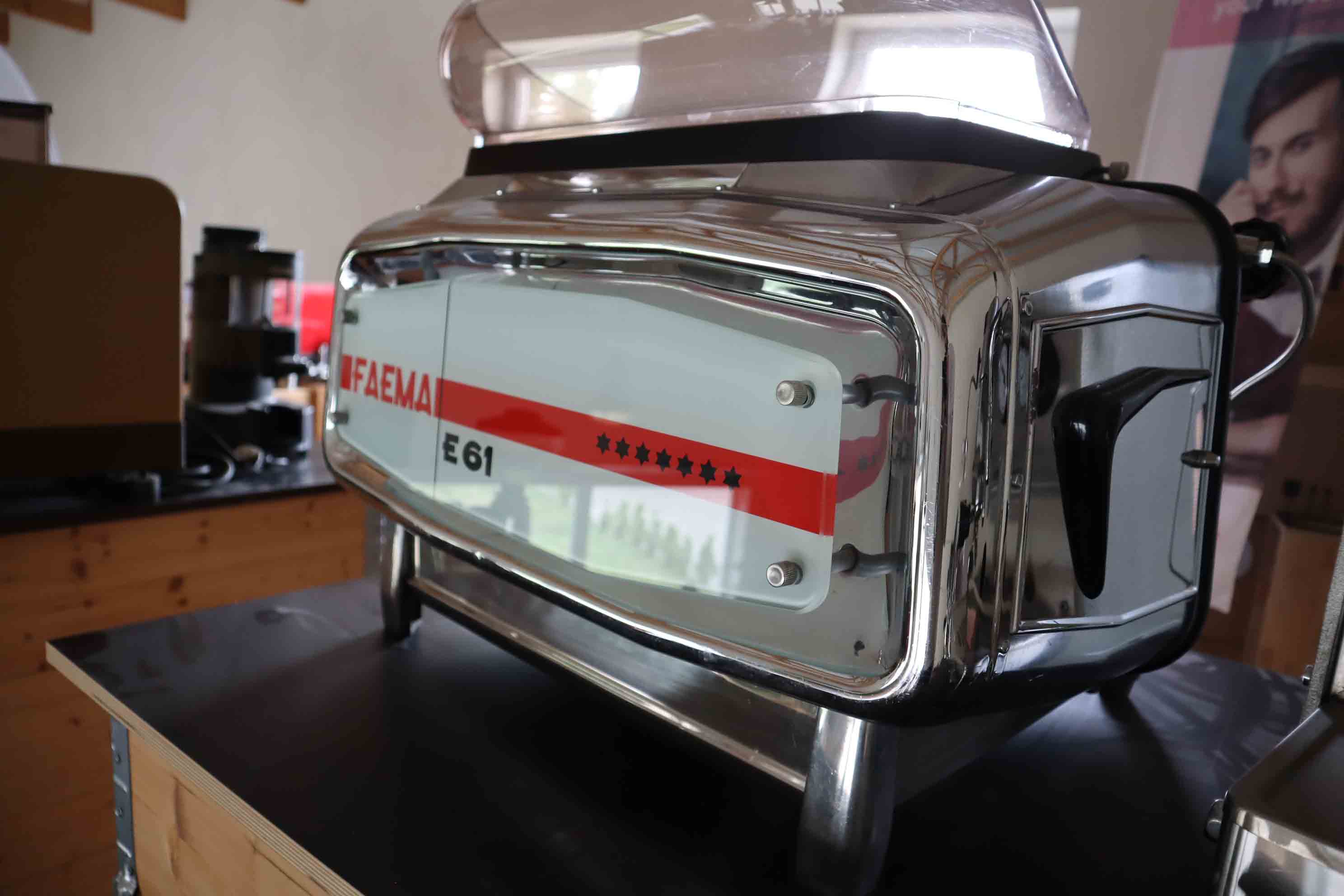 Close-up of a shiny stainless steel Faema E61 espresso machine on a black countertop.