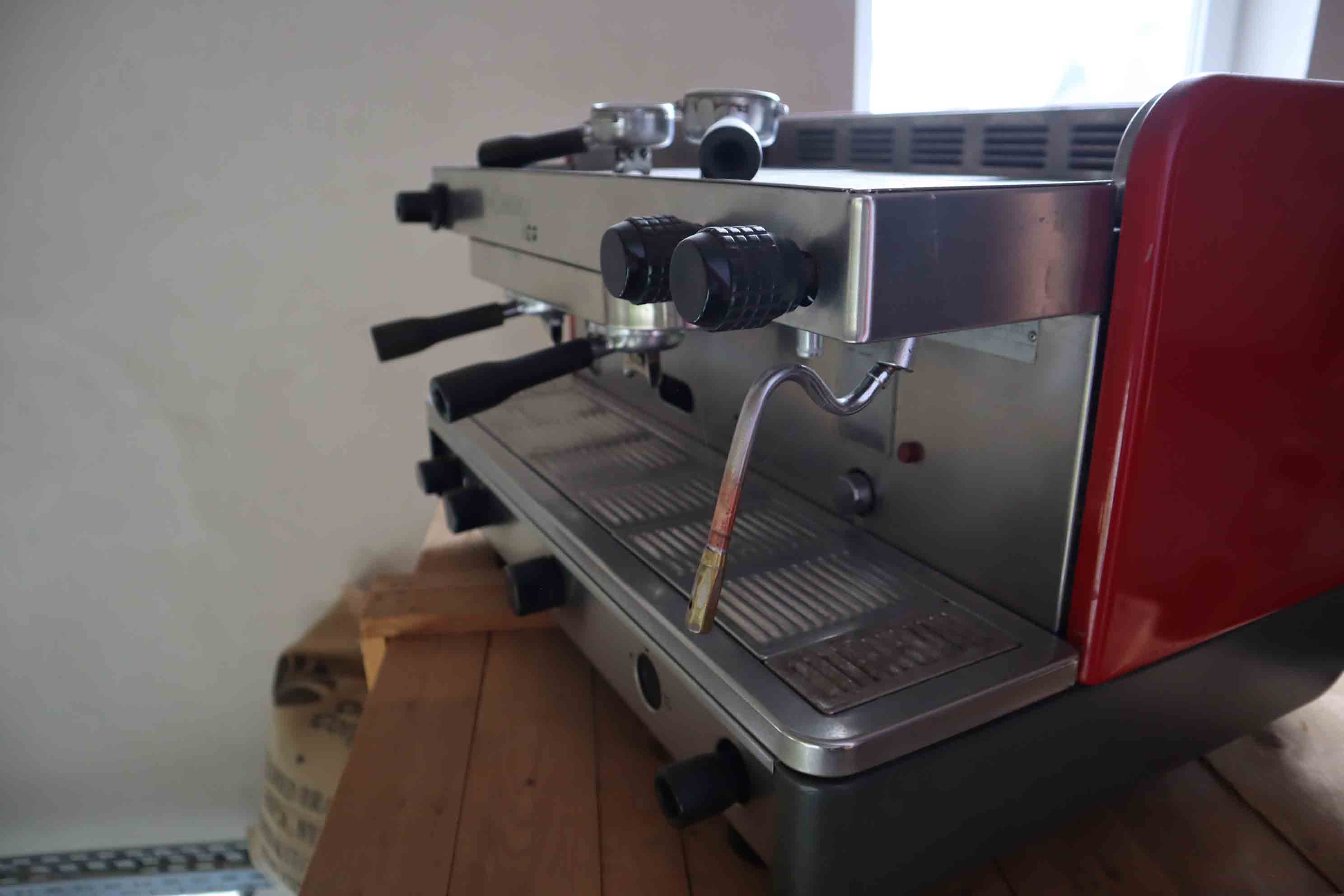 Close-up of a stainless steel and red espresso machine with black knobs on a wooden surface.