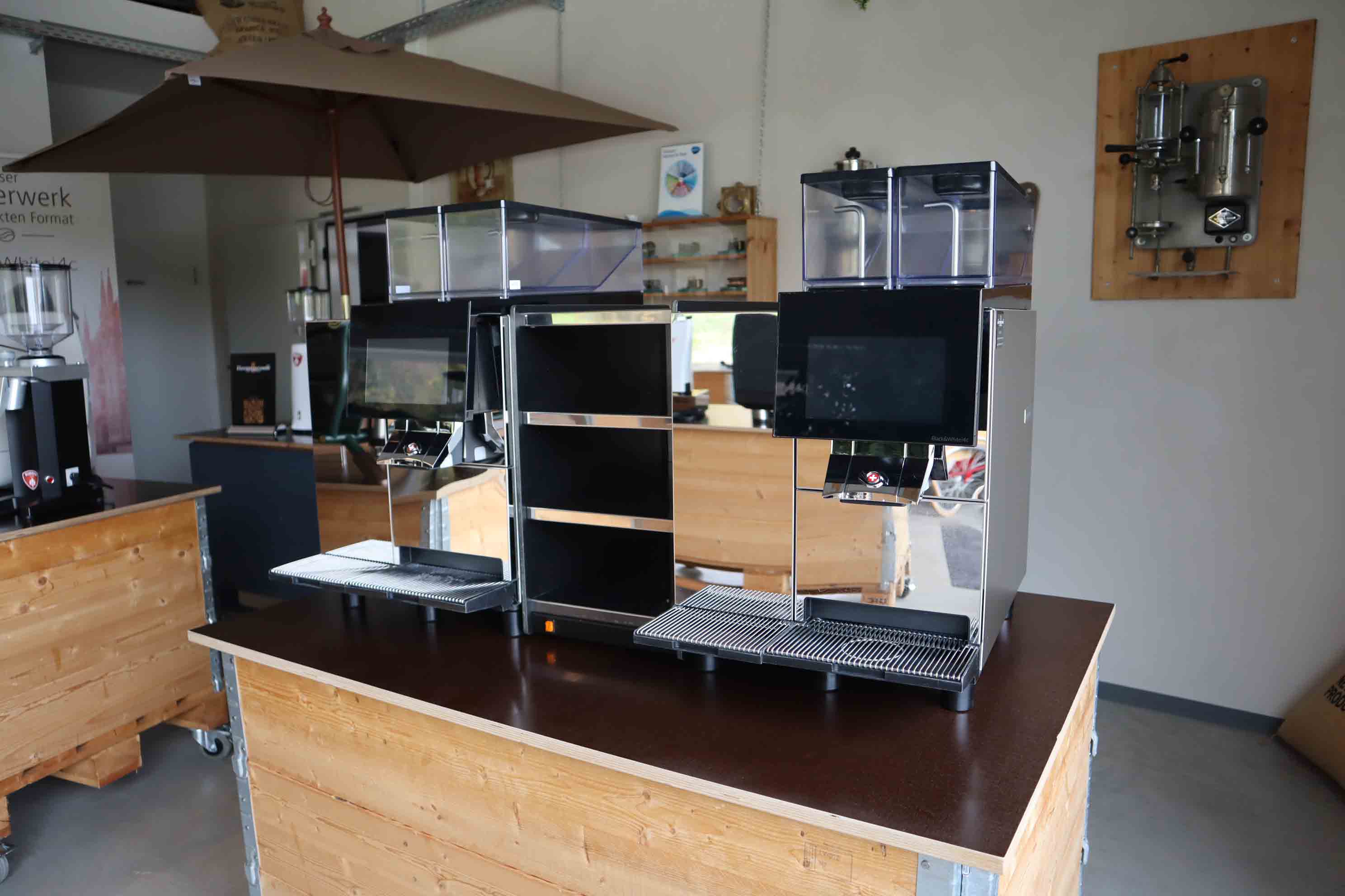 Two modern coffee machines with digital touch screens on a wooden counter in a clean, minimalist cafe interior.